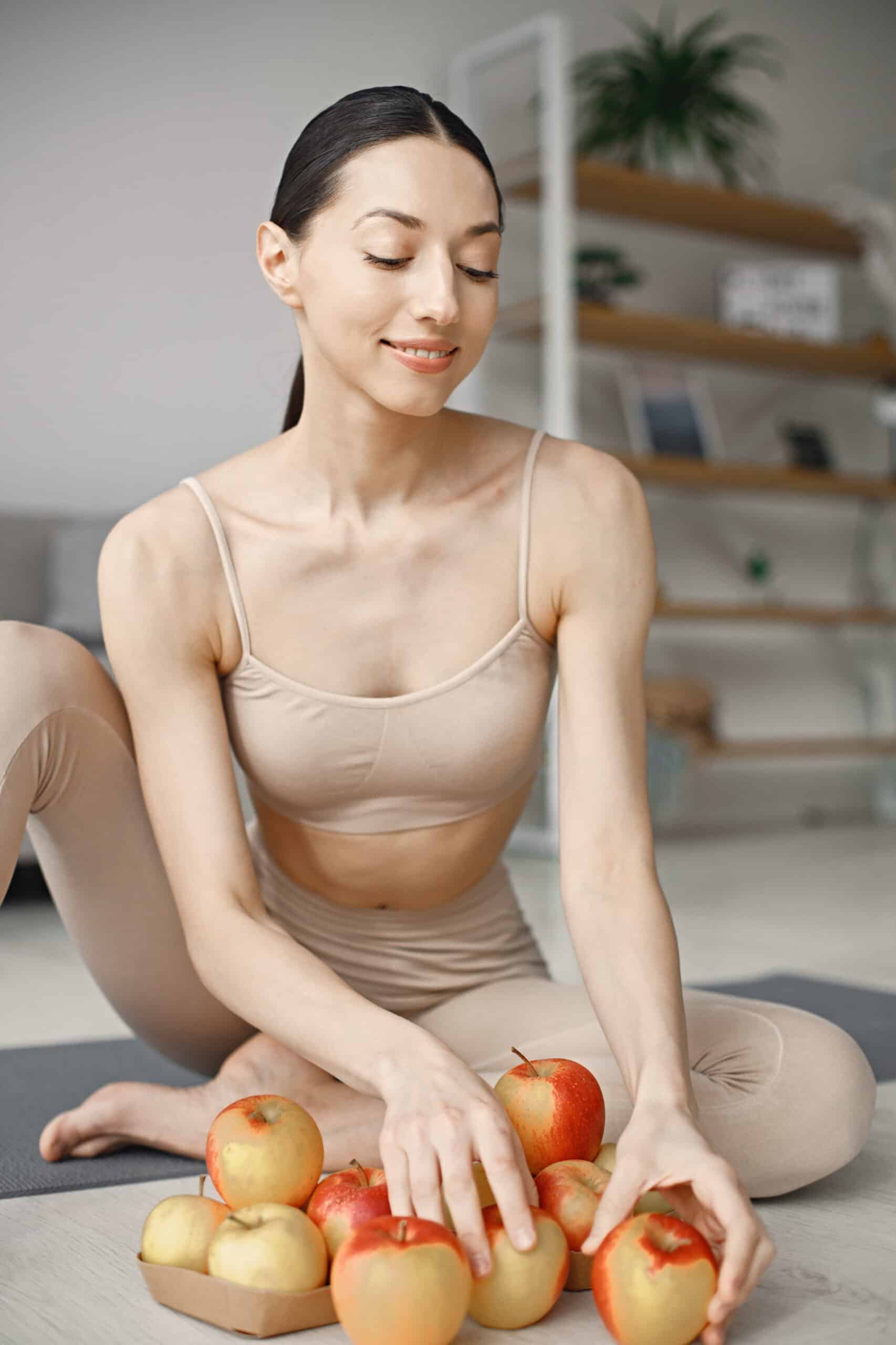 Young fitness woman sitting on yoga mat at home and holding fres